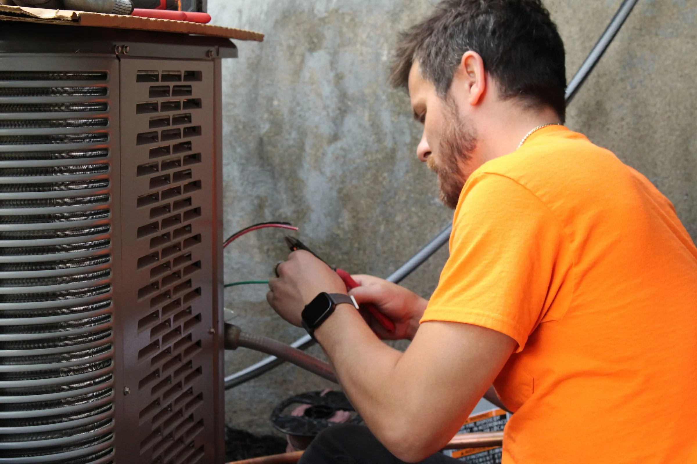 Technician handling red and green wires at an outdoor air conditioner condenser