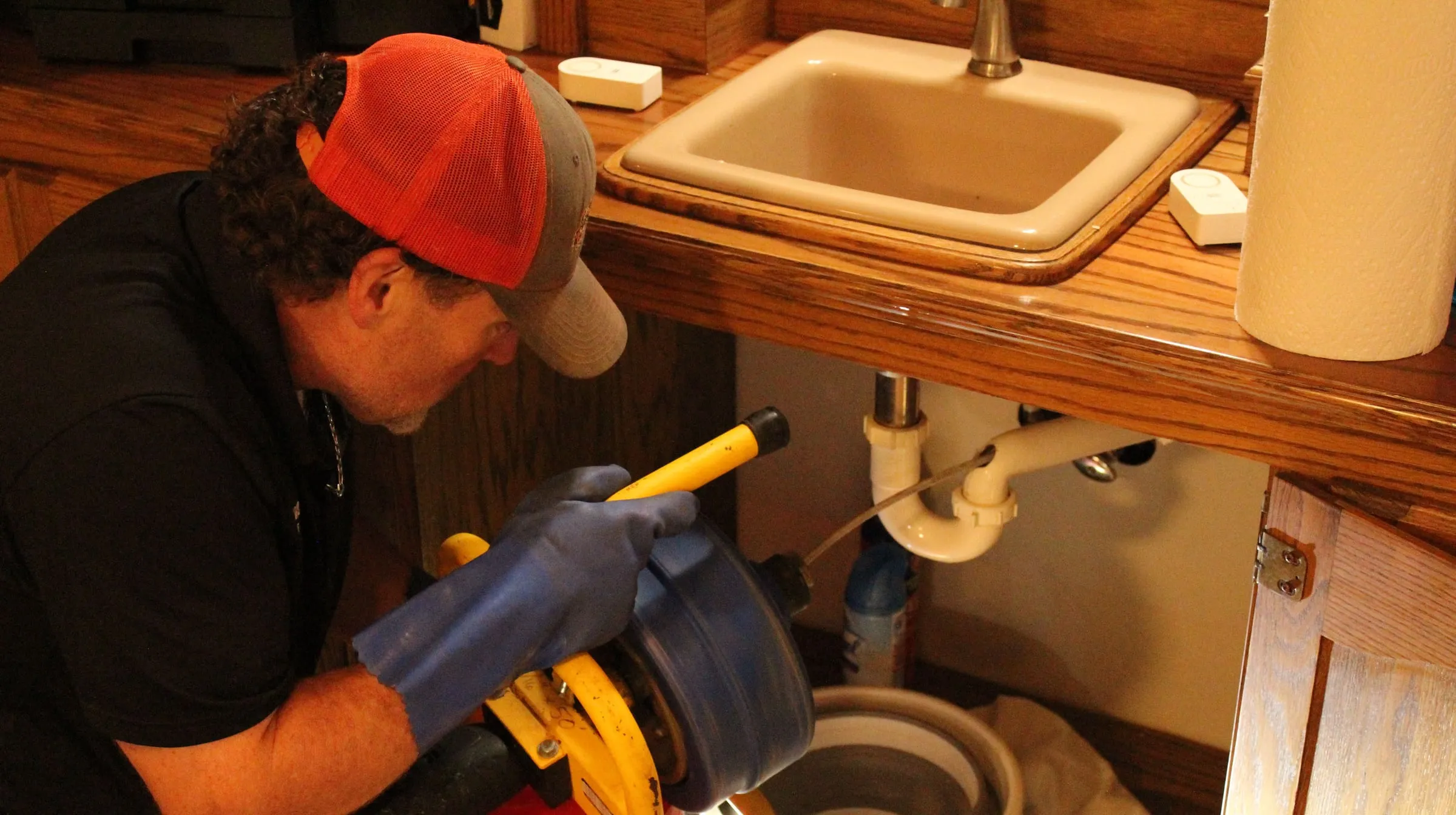 Technician feeding a drain machine cable into the pipe under a sink