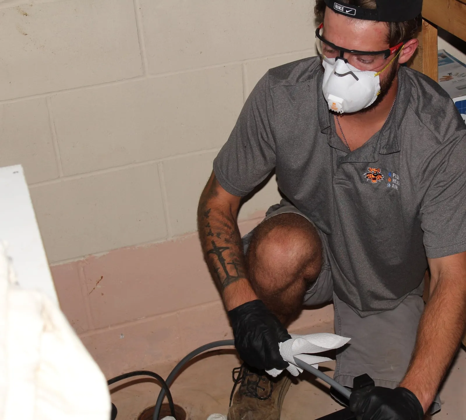 Tiger technician kneeling at a basement floor drain, wiping a drain camera cable
