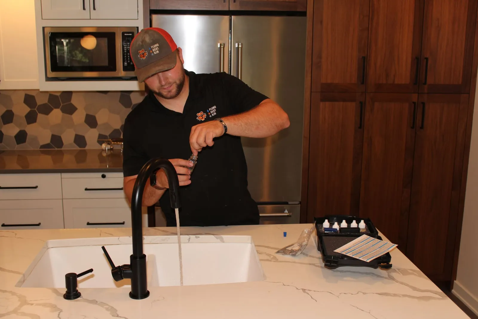 Tiger technician filling a sample vial at a kitchen faucet beside a water test kit
