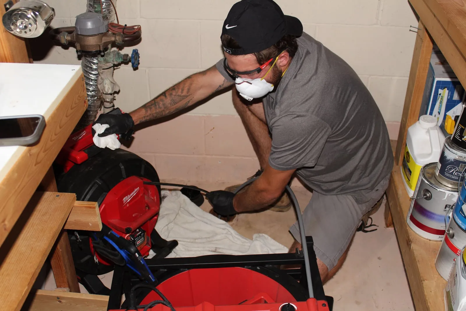 Technician kneeling on a basement floor, working a drain machine at a floor drain