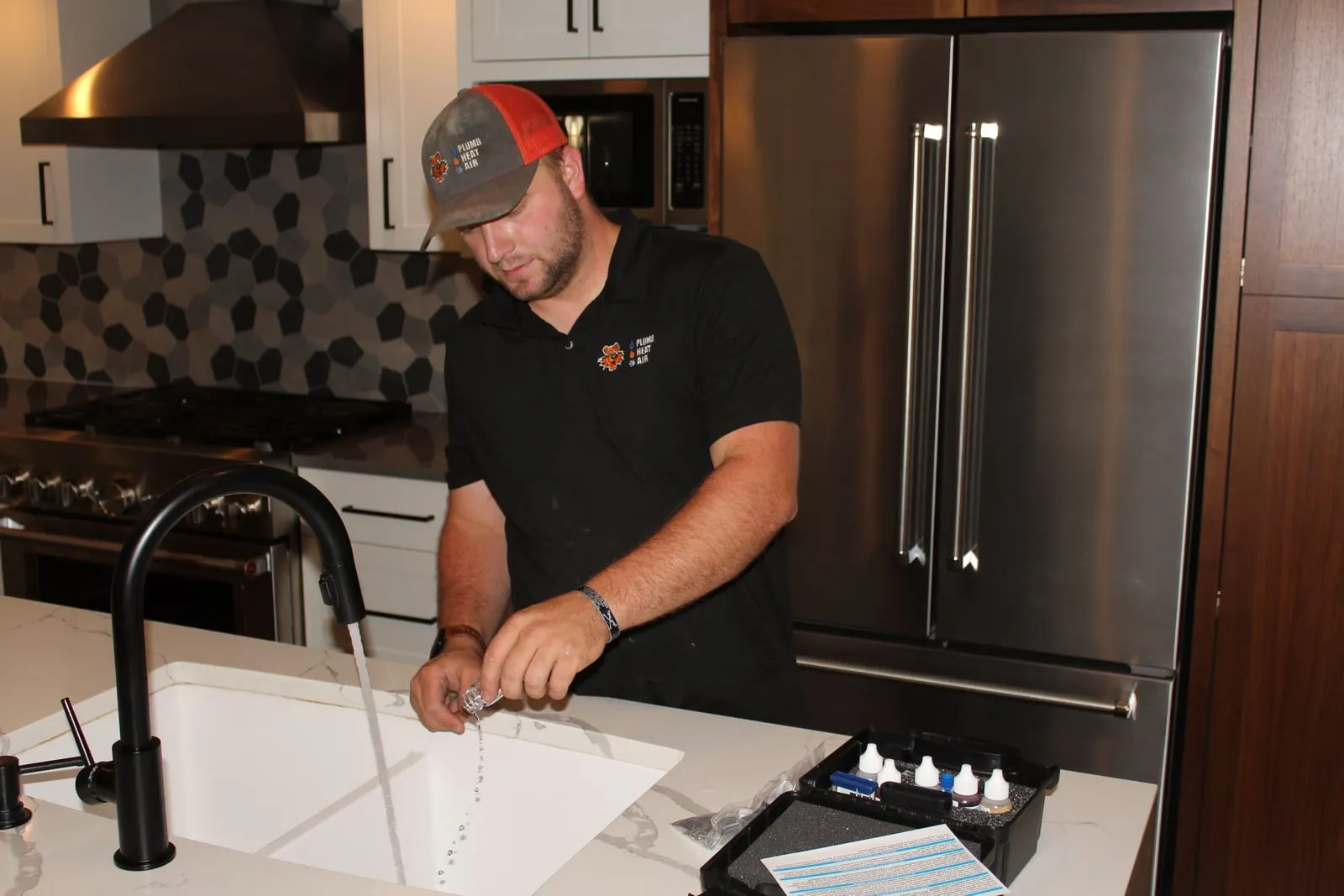 Tiger technician rinsing a sample vial at a kitchen faucet beside a water test kit