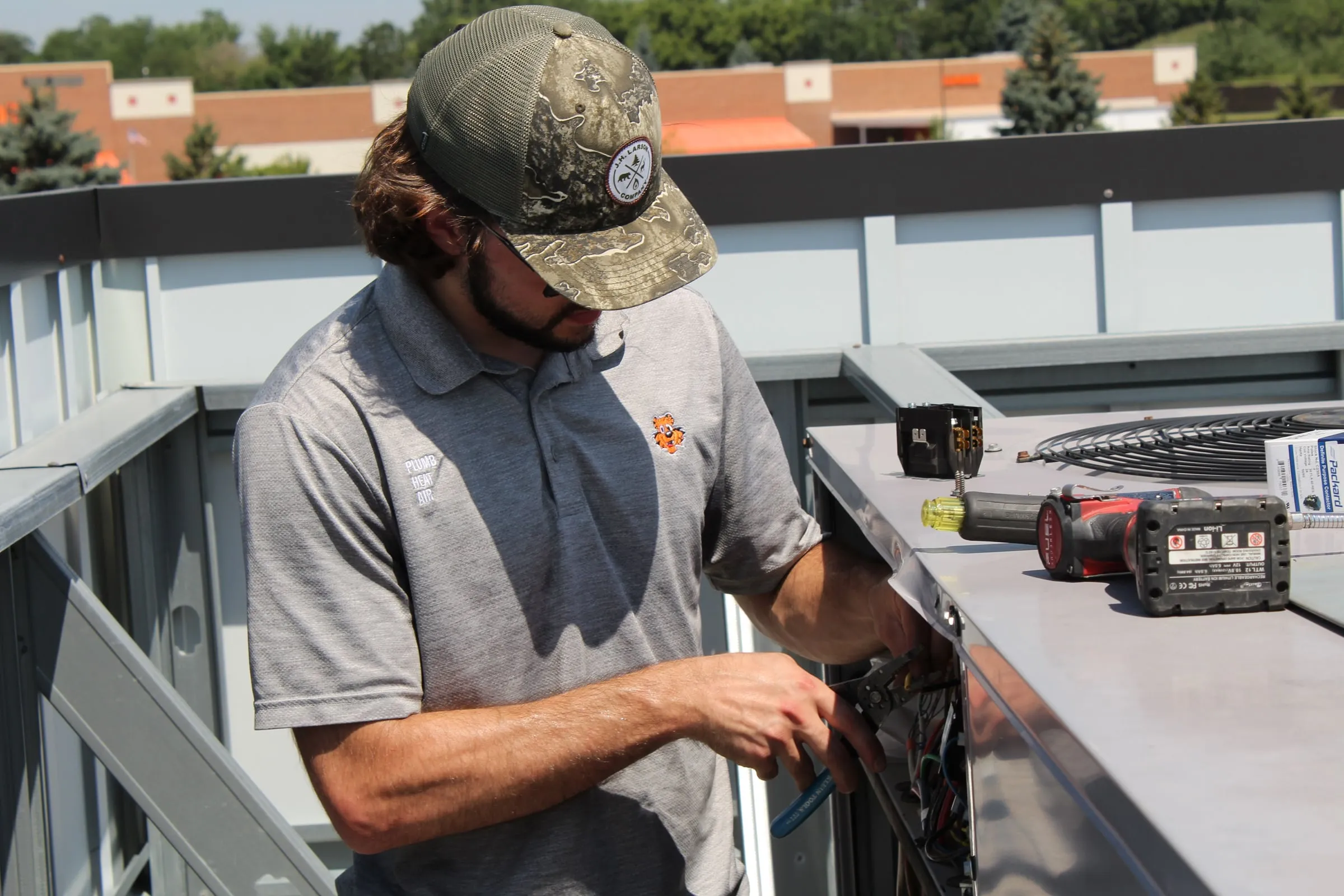 Tiger technician using pliers on wiring inside a commercial rooftop unit