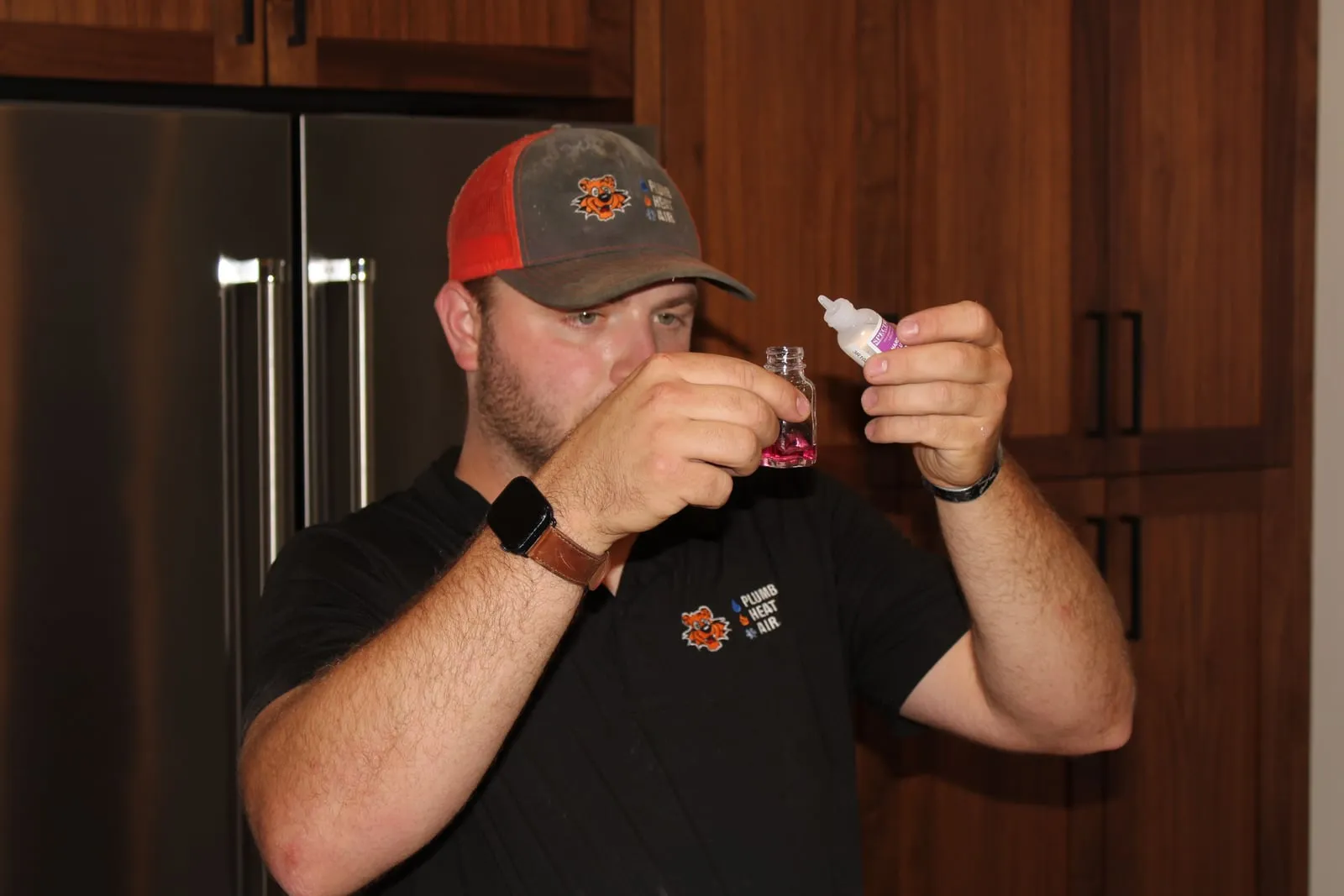 Tiger technician holding up a vial of pink-tinted water during a water test in a kitchen