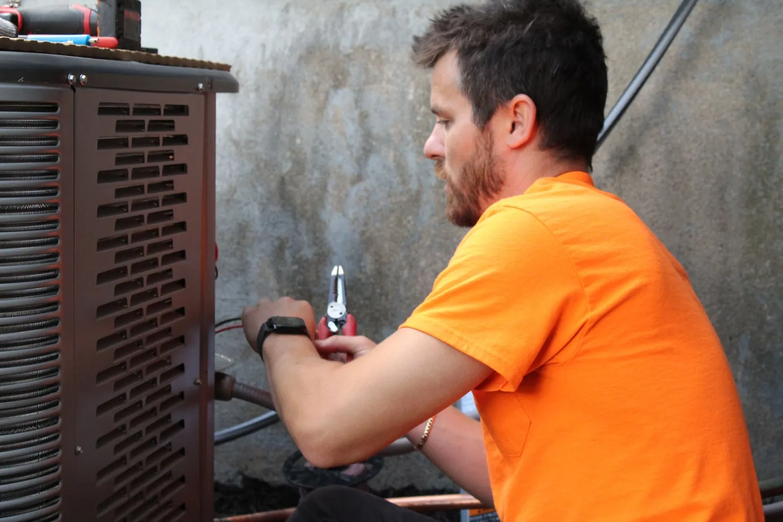 Technician holding wire strippers while working at the side of an outdoor air conditioner condenser