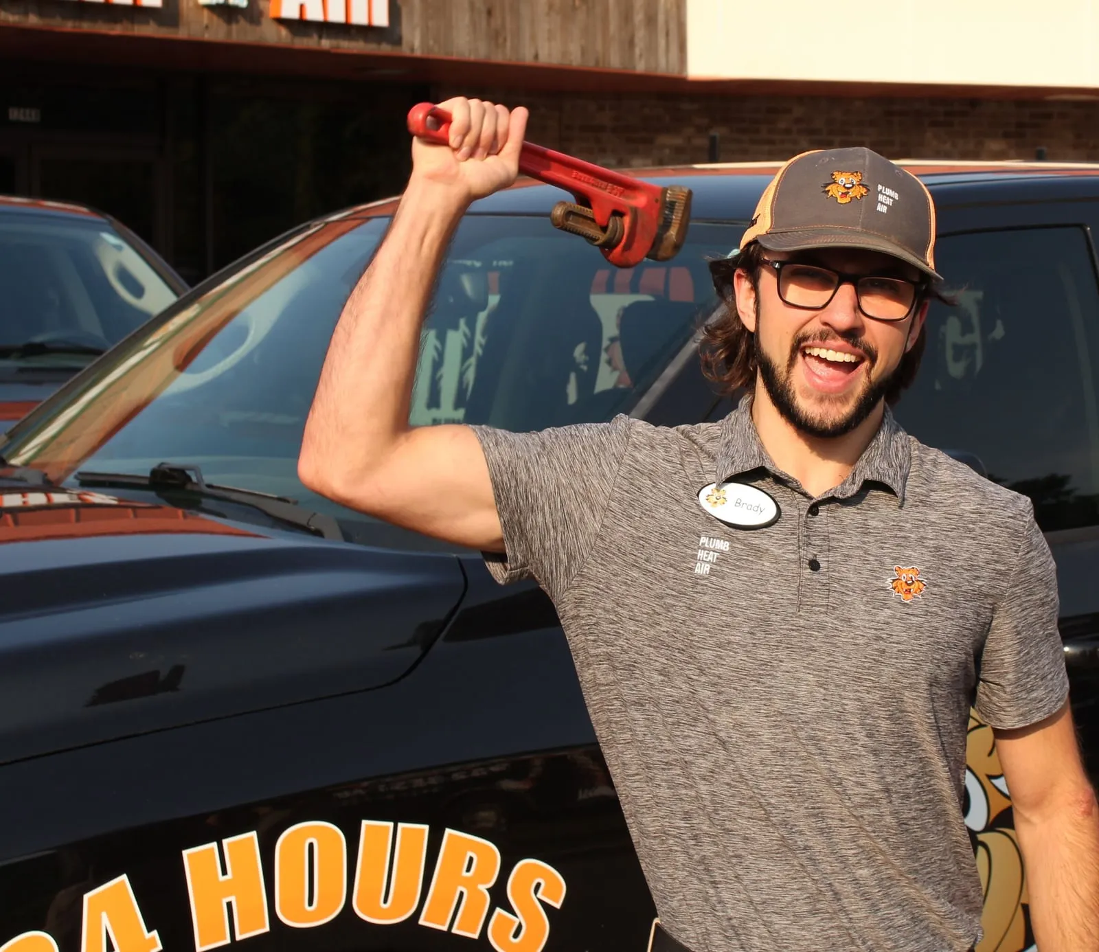 Laughing Tiger technician raising a red pipe wrench in front of a Tiger truck