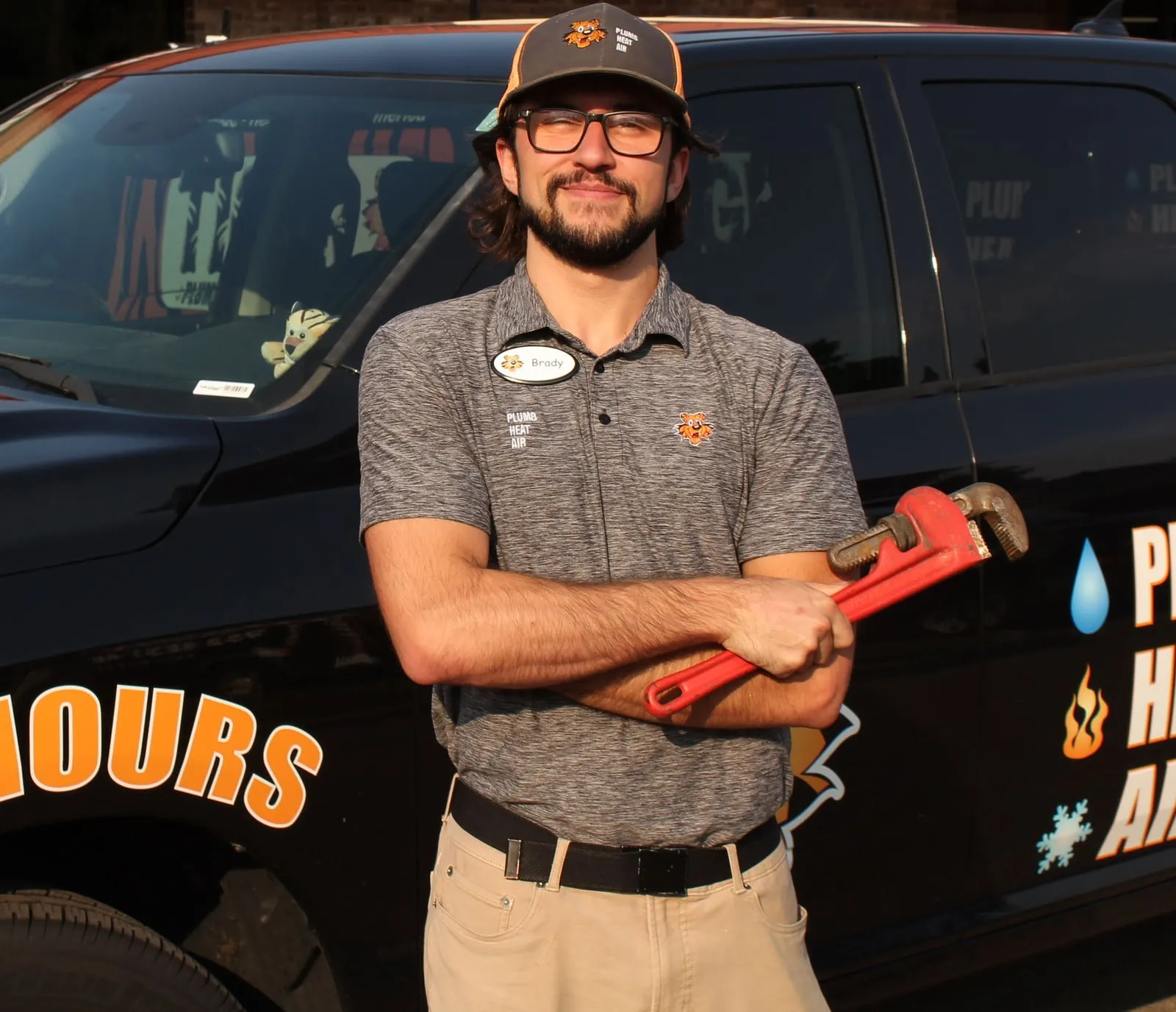 Tiger technician with arms crossed, holding a red pipe wrench in front of a Tiger truck