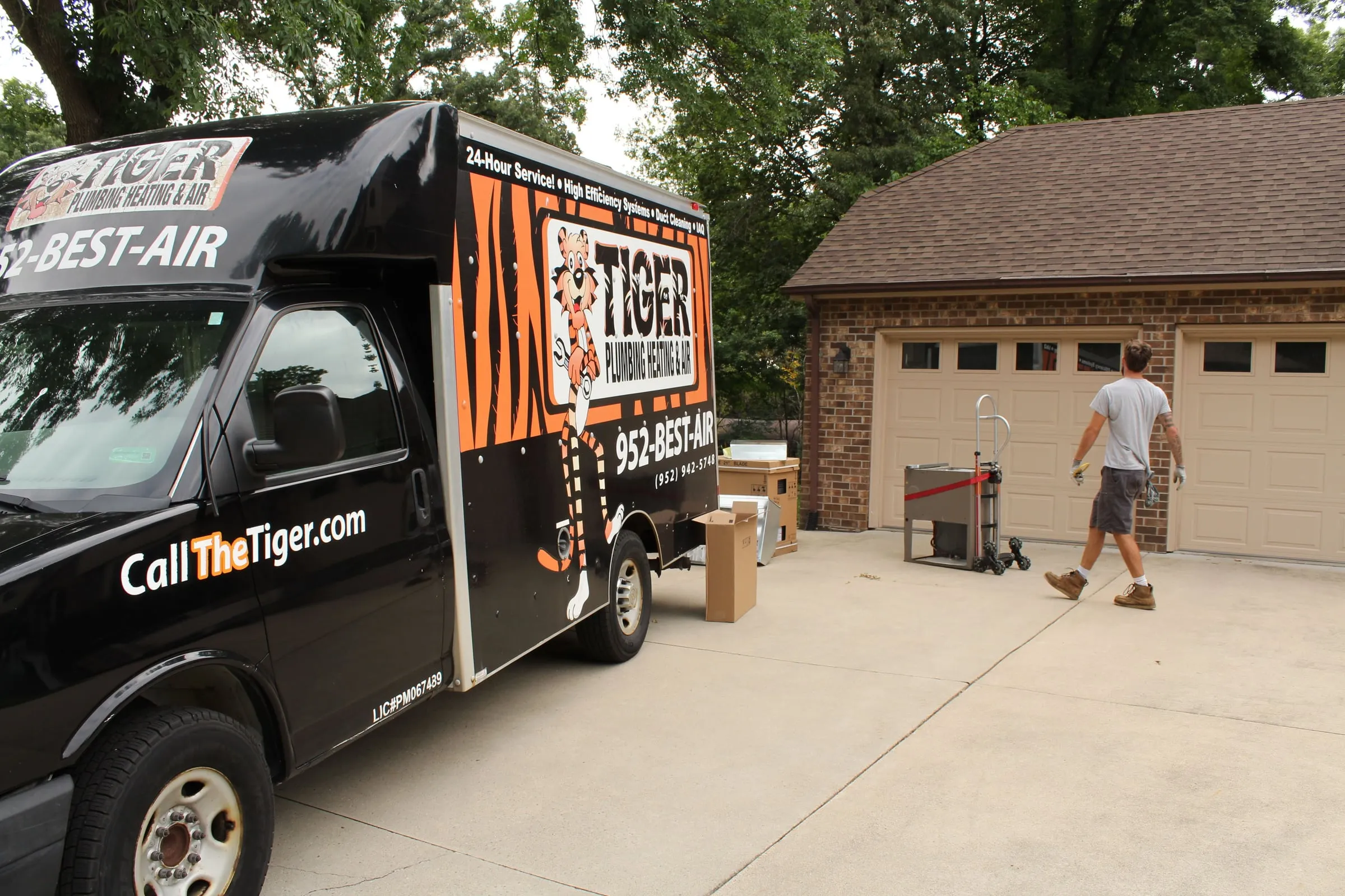 Tiger box truck on a driveway with boxed equipment and a worker walking toward a garage