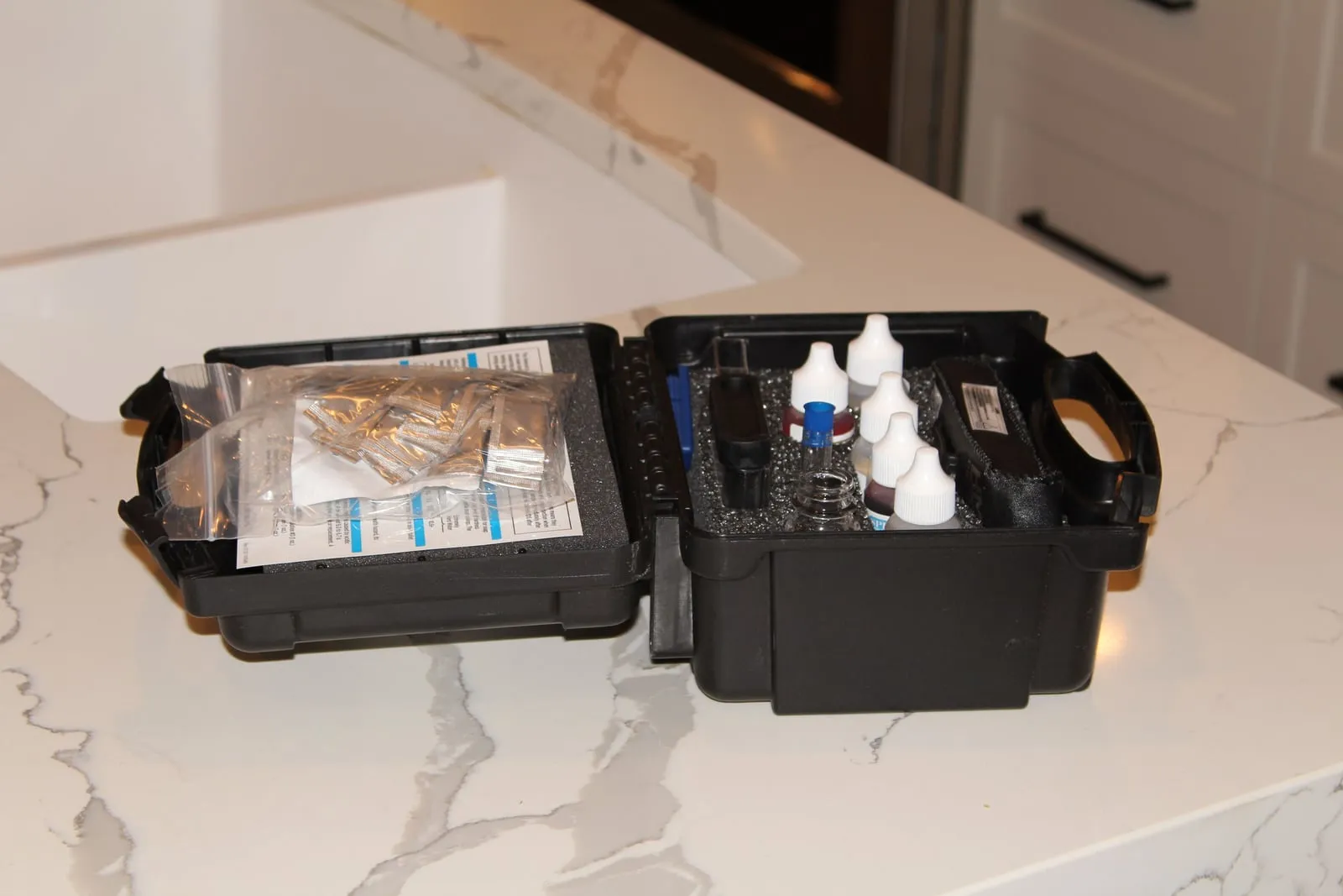 Open water test kit with reagent bottles and a sample vial on a kitchen counter